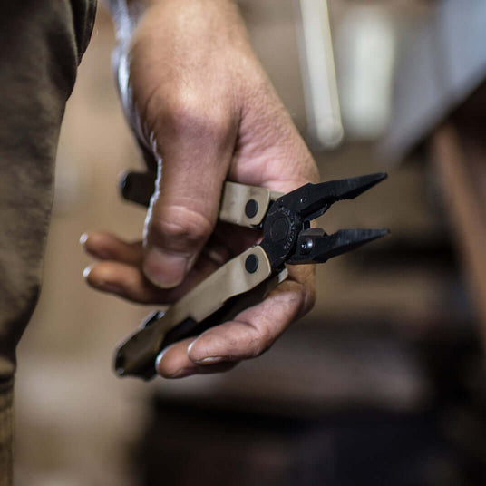 Translation missing: en.Close-up of a hand holding a Coyote Tan Leatherman Rebar® multitool with pliers, showcasing its rugged design