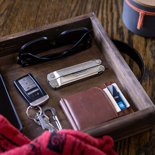 Translation missing: en.Stainless Steel Leatherman Bond® and accessories on a wooden tray, including keys, sunglasses, and a wallet