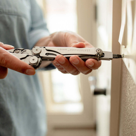 Translation missing: en.Someone using a Stainless Steel Leatherman Wave® Plus multi-tool with a flat bit to screw into a wall
