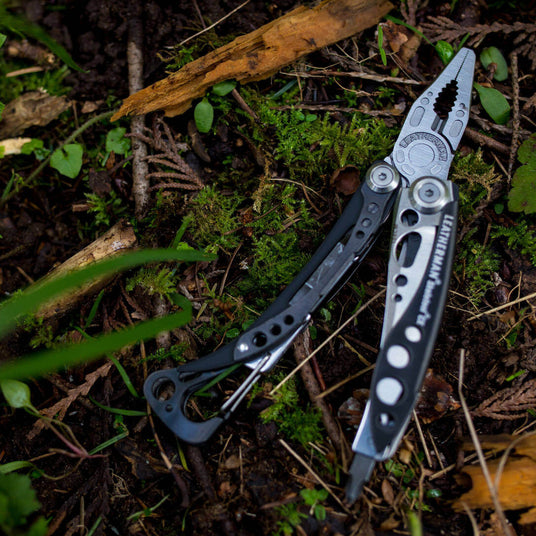 Translation missing: en.Black & Stainless Skeletool® CX multitool resting on mossy forest floor, showing its sleek design and versatility