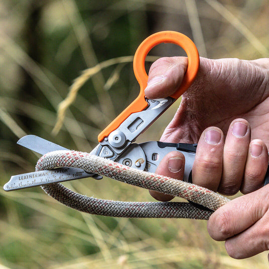 Translation missing: en.Orange/Black Leatherman Raptor® Rescue tool cutting through rope, ideal for emergency situations and rescue operations