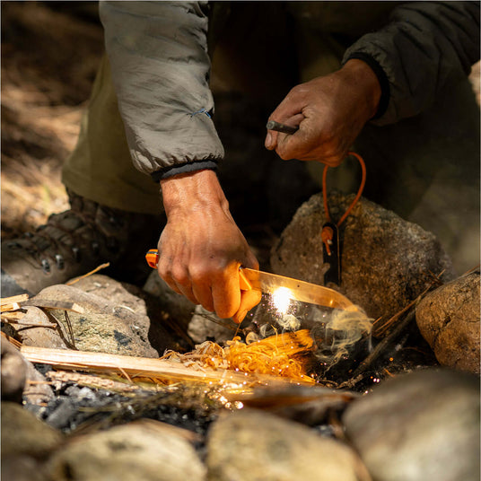 Translation missing: en.A person using an Orange Pop Leatherman Pioneer™ knife to start a fire in a camping setting