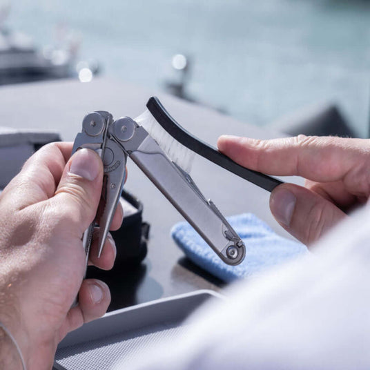 Translation missing: en.Close-up of hands using a brush to clean a Stainless Steel Leatherman Wave® Plus multitool outdoors