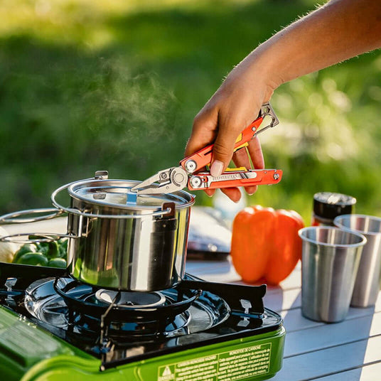 Translation missing: en.Person using a Guava Leatherman Signal® multitool while cooking on a camping stove with vegetables