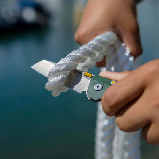 Translation missing: en.Person using an Evergreen Leatherman Glider® knife to cut through thick white rope near water