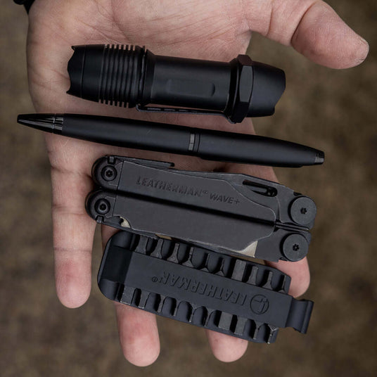 Translation missing: en.Black Leatherman Wave® Plus multi-tool, Leatherman bit kit, flashlight, and pen in a hand, showcasing handy outdoor gear