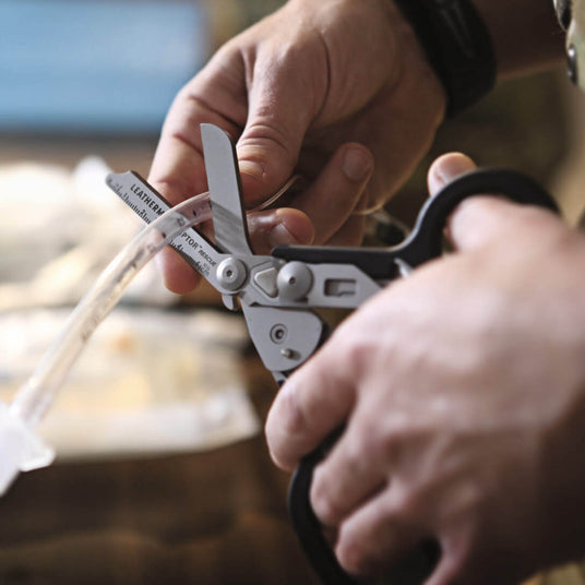 Translation missing: en.Close-up of hands using a Black Leatherman Raptor® Rescue shears on a medical tube for emergency situations