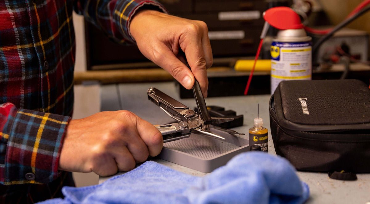 Person cleaning a stainless steel Leatherman Wave® Plus multitool on a workbench using the Leatherman Maintenance Kit.