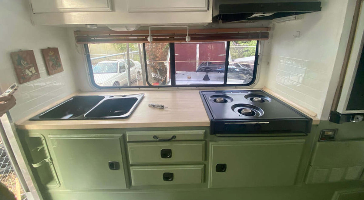 Modern camper kitchen with double sink, gas stove, and ample storage, featuring a bright and spacious layout with a Stainless Steel Leatherman Skeletool® on top.