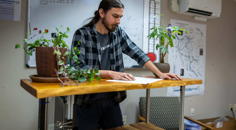 Translation missing: en.Seth Durham analyzing documents at a wooden table surrounded by plants in an office setting