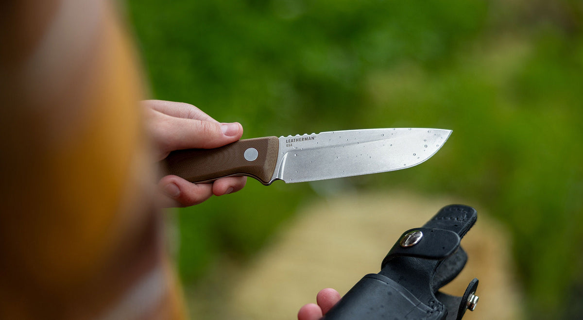 A hand holding the Leatherman TRAC fixed blade knife and sheath