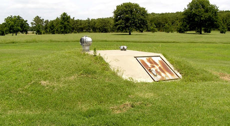 Translation missing: en.A concrete access hatch set in a grassy area, surrounded by trees, likely leading to an underground bunker