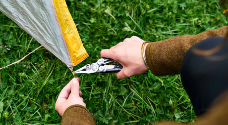 Translation missing: en.Person setting up a tent with a black and stainless Leatherman Signal
