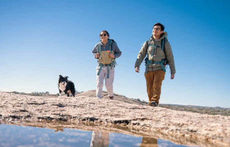 Translation missing: en.Two hikers and a dog exploring a rocky landscape with blue skies in the background