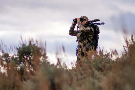 Translation missing: en.Hunter using binoculars in the wilderness while equipped with hunting gear for various outdoor activities