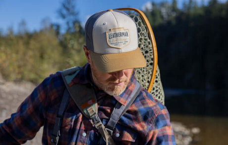 Translation missing: en.Man wearing a Natural/Gold Leatherman Pacific Northwest Trucker Hat while fishing in a scenic outdoor setting
