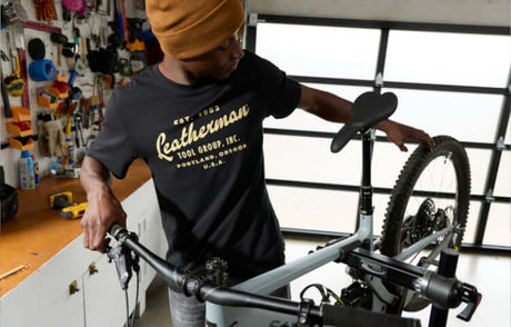 Translation missing: en.Man wearing a black Leatherman Vintage Tee, working on a bicycle in a well-equipped garage