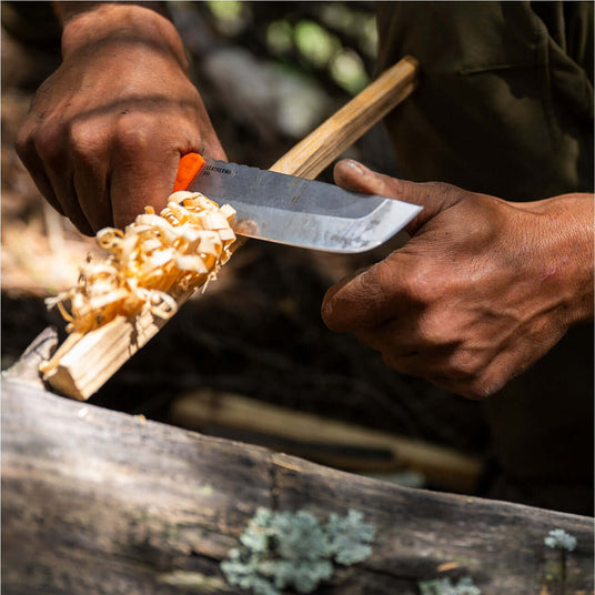 Translation missing: en.Close-up of hands using an Orange Pop Leatherman Pioneer™ knife to carve wood shavings outdoors
