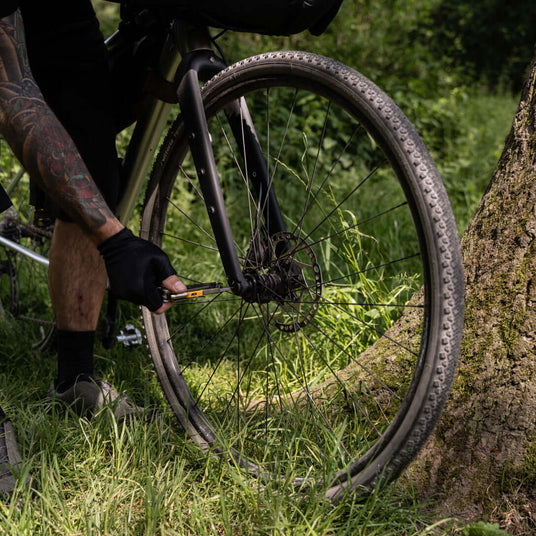 Translation missing: en.A cyclist using a Leatherman Signal® multi-tool to fix a bike tire in a lush, green outdoor setting