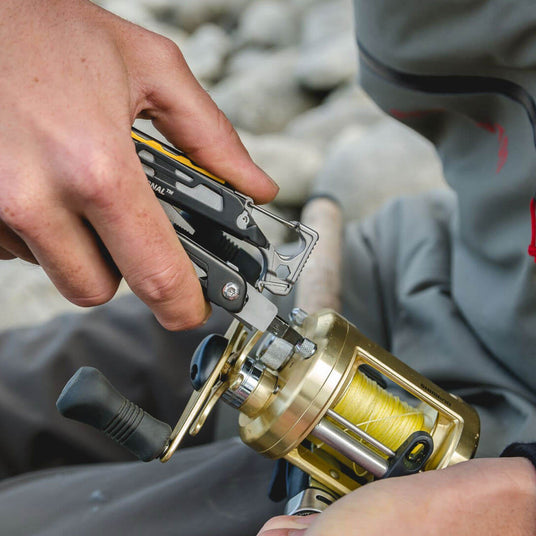 Translation missing: en.A person using a Black &amp; Stainless Leatherman Signal® multitool to fix a fishing reel