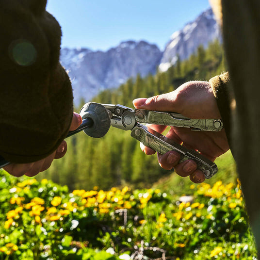 Translation missing: en.Hands using a customized Stainless Steel Leatherman Rebar® multitool outdoors with mountains in the background