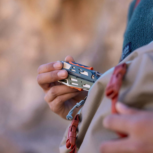 Translation missing: en.Person holding a Tundrascape Leatherman Signal® multitool near a backpack, perfect for outdoor adventures