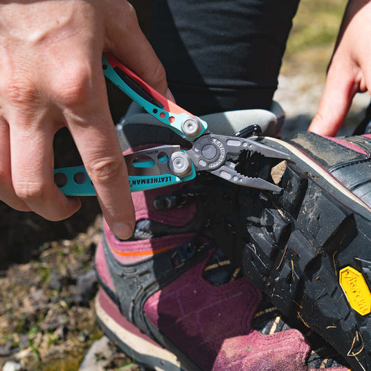 Translation missing: en.Person using a Paradise Leatherman Skeletool® CX multitool for outdoor repair on hiking boots