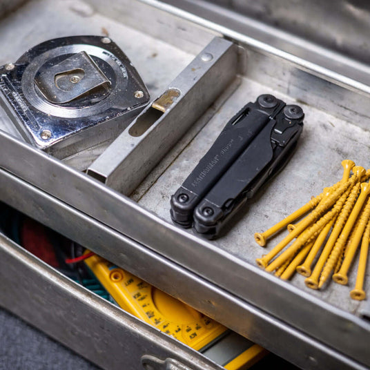 Translation missing: en.Black Leatherman Surge® multi-tool alongside measuring tape and screws in a toolbox