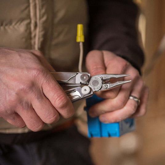 Translation missing: en.Man using a Stainless Steel Leatherman Wave® Plus multi-tool for electrical work in a wooden environment