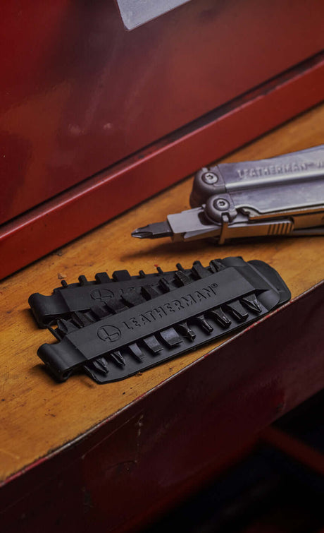 Translation missing: en.Leatherman Bit Kit Set laying on a wooden surface alongside a Stainless Steel Leatherman Wave® Plus with a bit attached