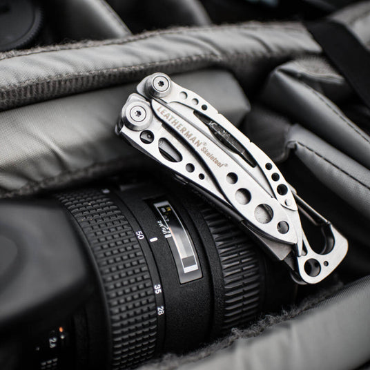 Translation missing: en.Stainless Steel Leatherman Skeletool® resting on top of a camera lens in a gear bag