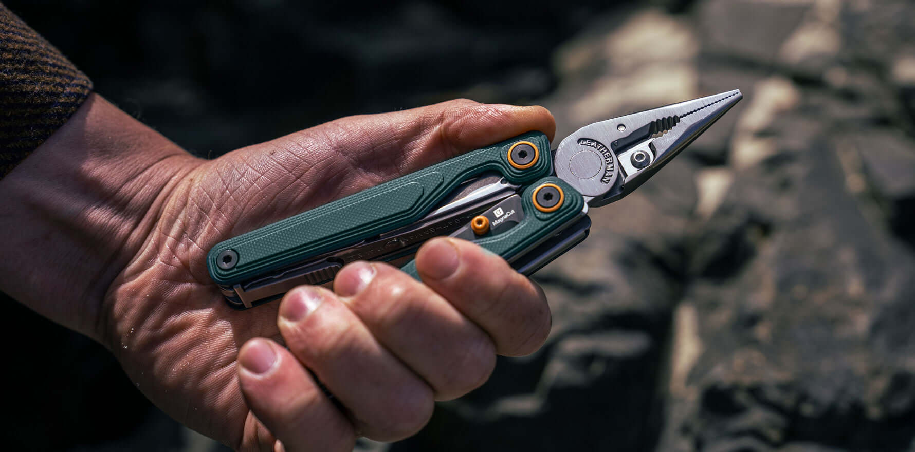 A person holding a Cascadia Leatherman Wave® Alpha multitool pliers against a rocky background.