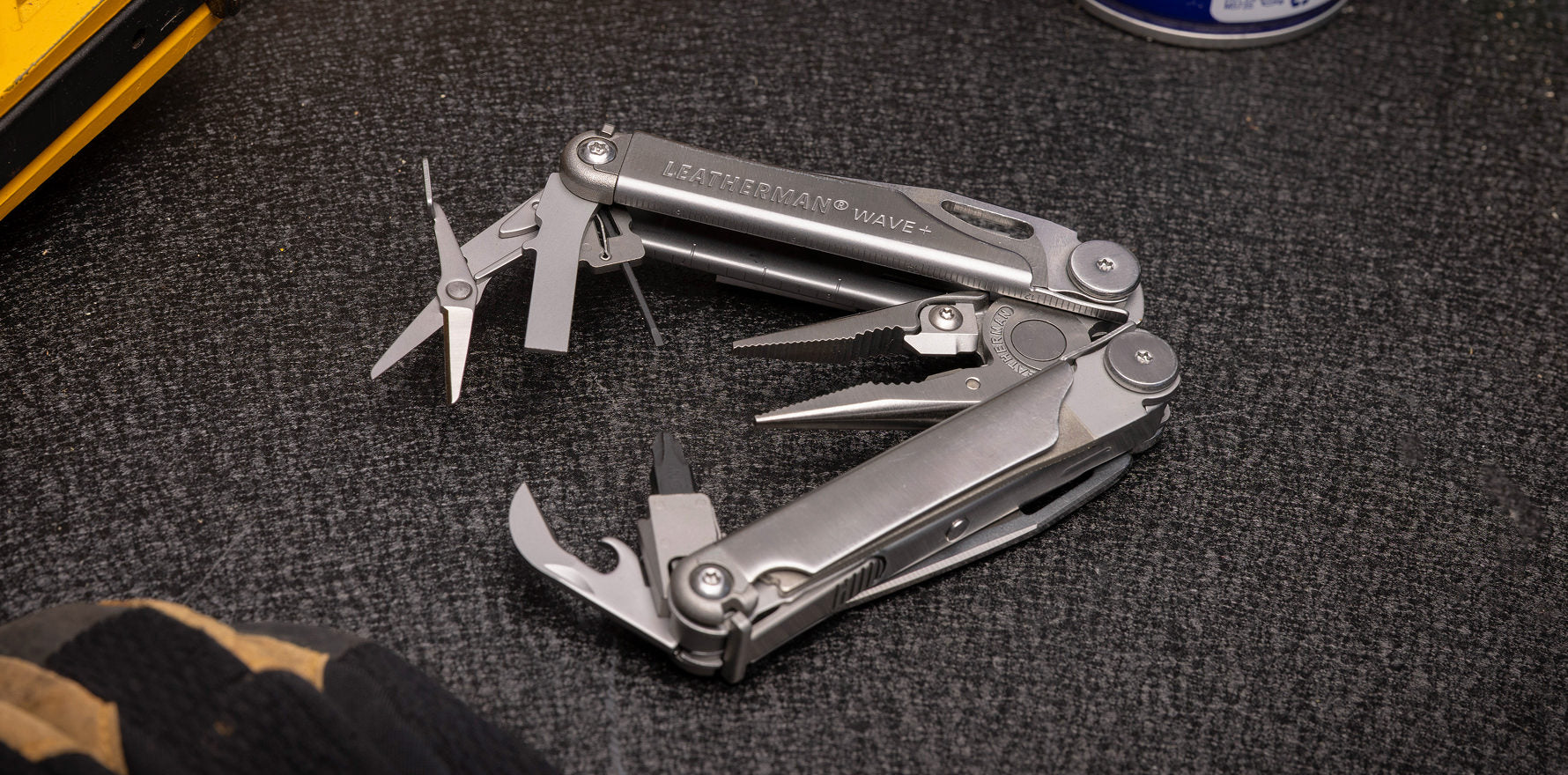 Stainless steel Leatherman Wave® Plus multi-tool opened on a work table, showcasing various tools and features.