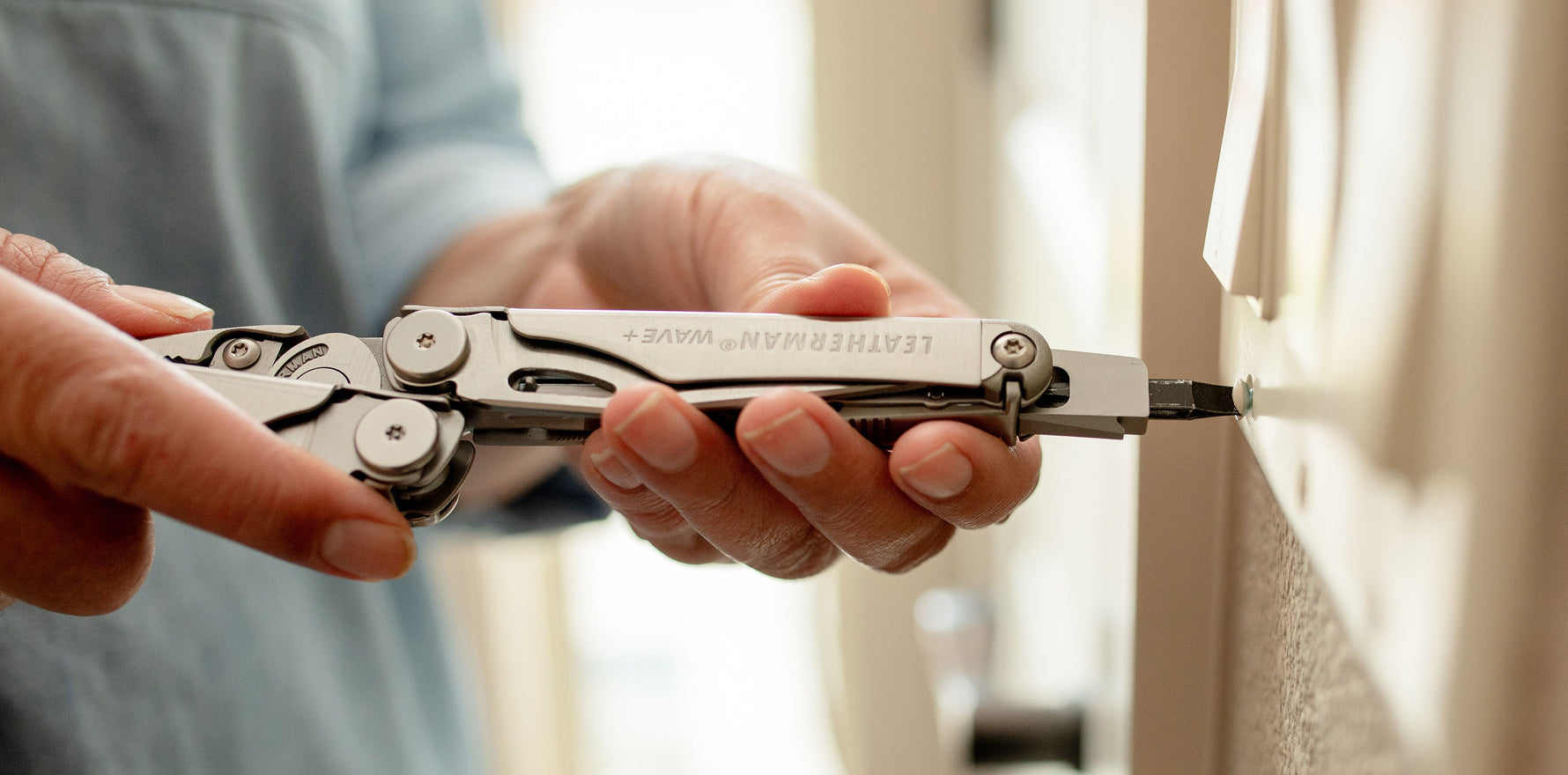 Person using a stainless steel Leatherman Wave® Plus large bit driver to attach a screw to a light switch.