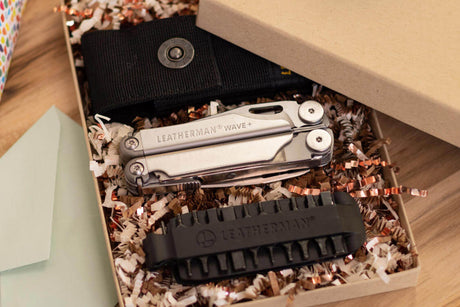 Translation missing: en.Stainless Steel Leatherman Wave® Plus closed in a gift box next to a sheath and a bit kit on a table