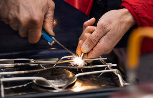 Translation missing: en.A person holds a sparkler to ignite a stove, creating a bright flame in a dimly lit kitchen