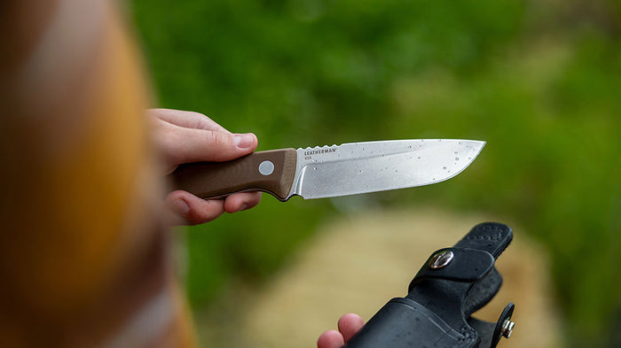 Translation missing: en.Person holding an Earth Brown Leatherman Trac™ knife with water drops on the blade, in a natural setting
