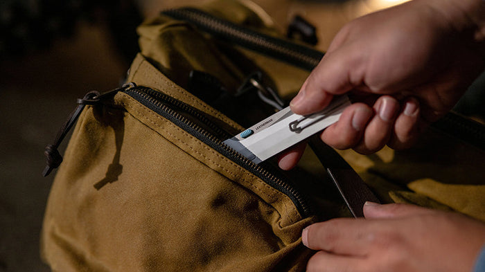 Translation missing: en.Hand retrieving the Alpine Leatherman Glider™ knife from a bag zipper, showcasing Leatherman’s all-new folding knife