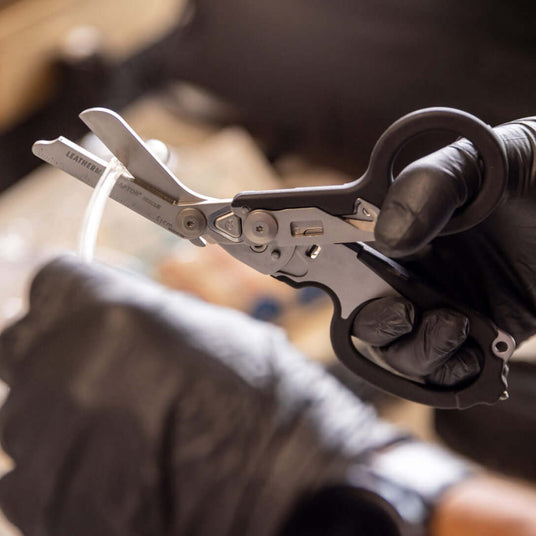 Translation missing: en.Close-up of a black Leatherman Raptor® Rescue tool in use, held by a gloved hand, showcasing its versatility