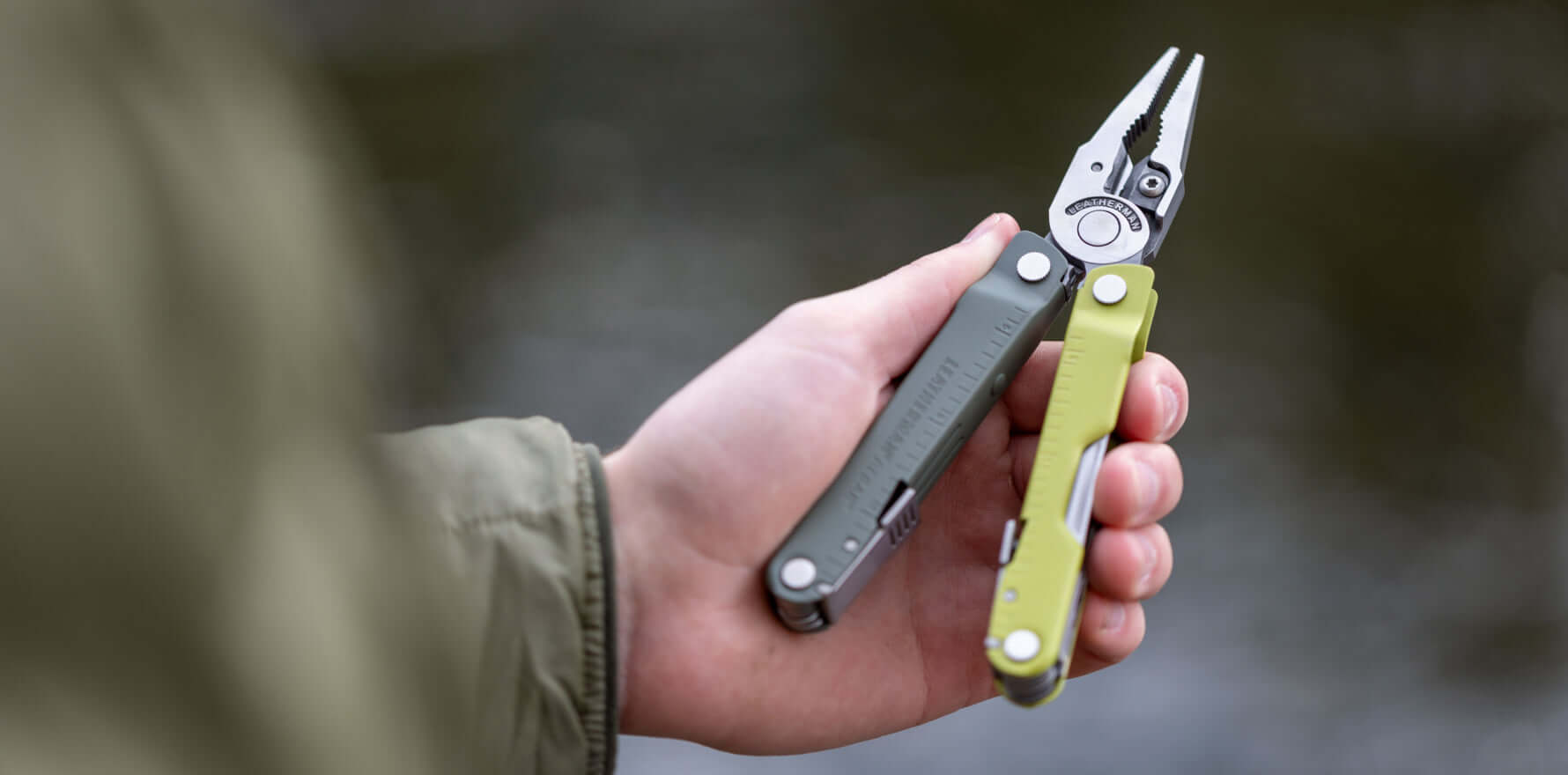 Person holding a Mossy Slate Leatherman Rebar® multi-tool, showing its pliers and colorful handles by the water.