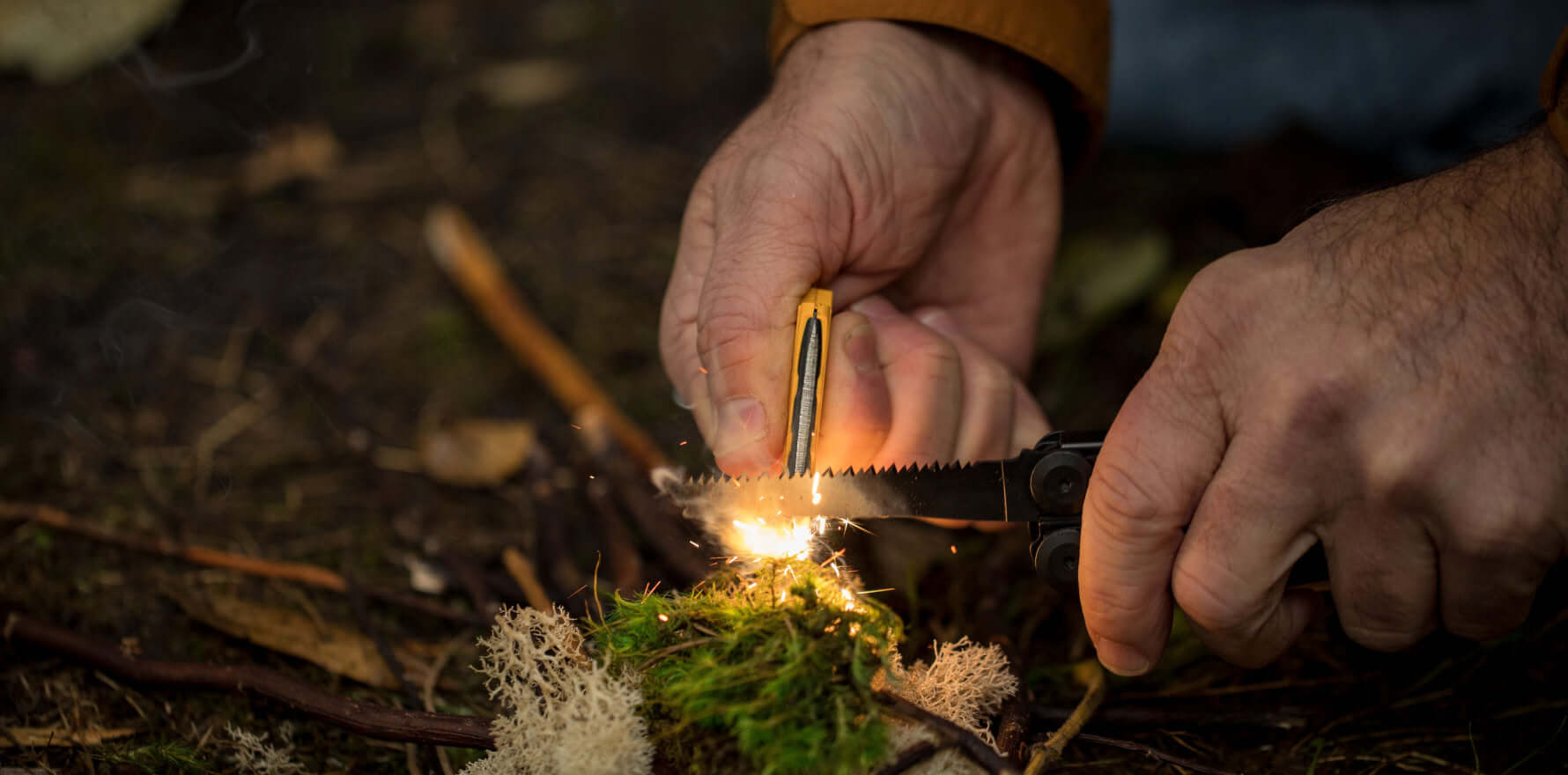 A person using the ferro rod on a  Leatherman Signal® to create sparks while preparing kindling in the forest.