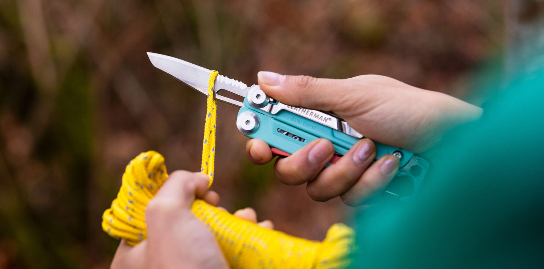 Person using an aqua and stainless Leatherman Signal® multitool to cut yellow rope outdoors.