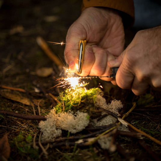 Translation missing: en.A person using the ferro rod on a Leatherman Signal® to create sparks while preparing kindling in the forest