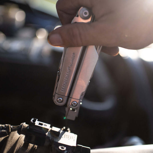 Translation missing: en.Stainless Steel Leatherman Surge® multitool in use on a vehicle engine, showcasing its versatility and functionality