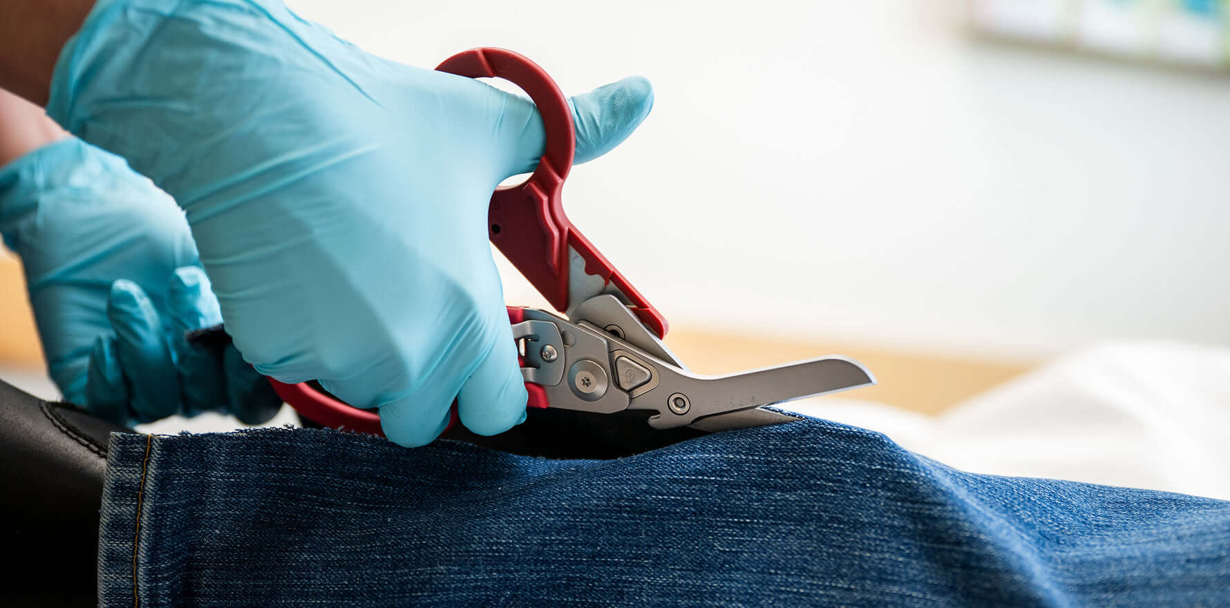 Person with blue gloves using a Red Leatherman Raptor® Rescue shears to cut a pant leg.