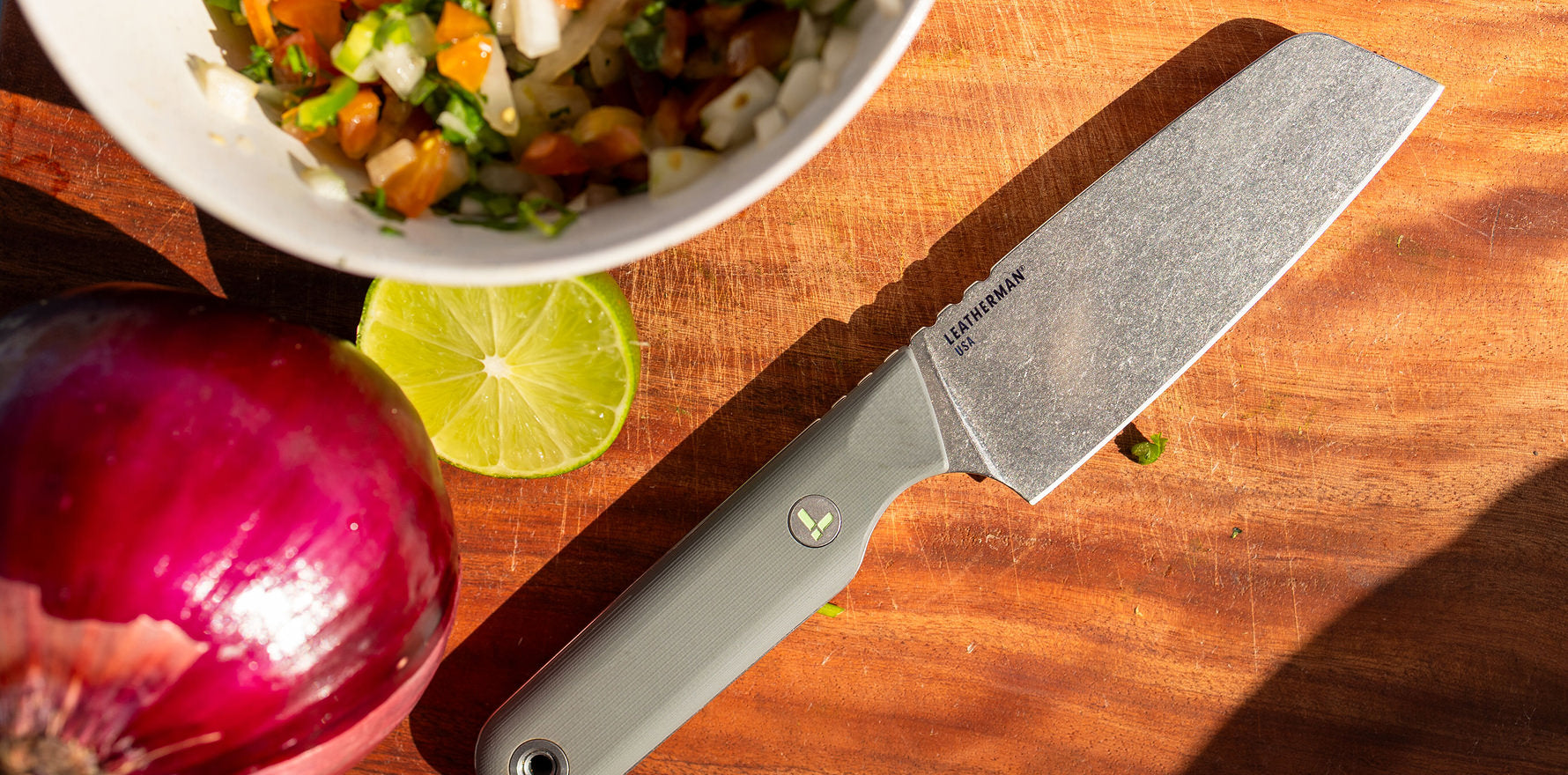 Vapor Grey Leatherman Rustle™ knife on a wooden cutting board with vegetables and lime.