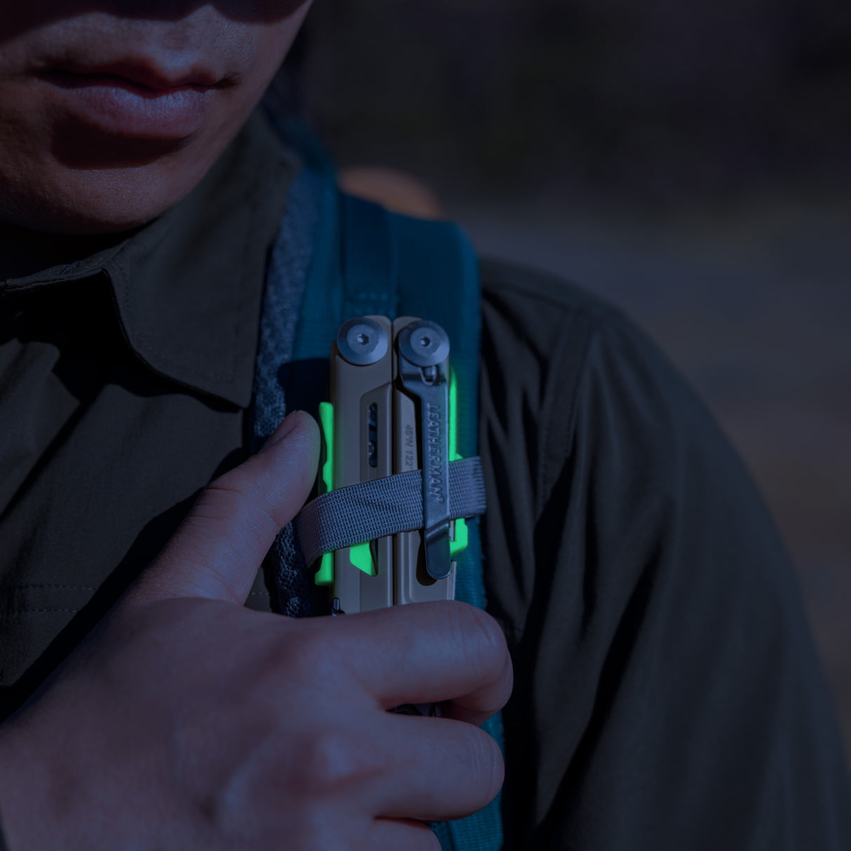 Translation missing: en.Person securing a Signal Sandstorm multitool with neon accents to a backpack strap outdoors